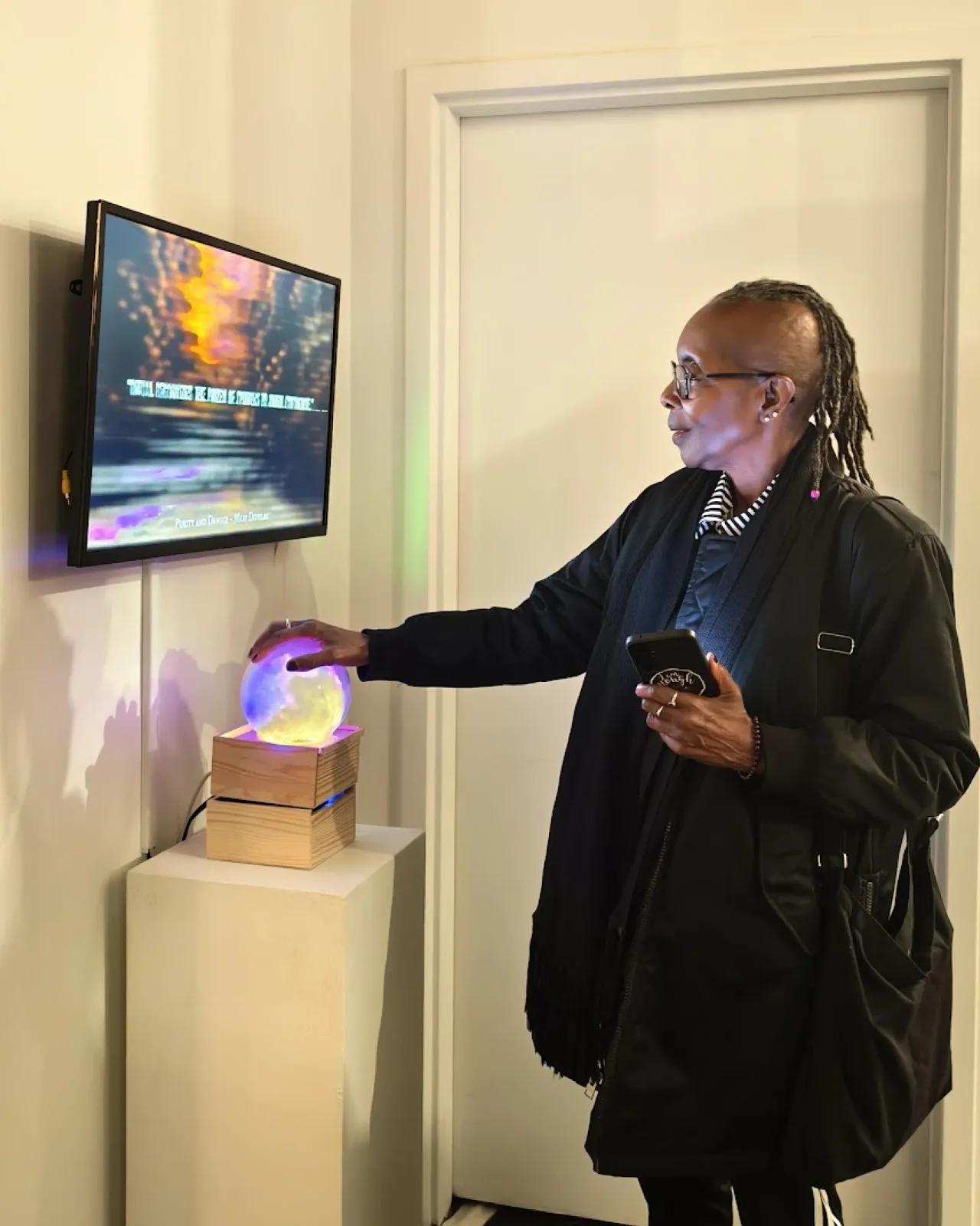 Gallery visitor extending a hand toward Vibe Altar, with its screen and pedestal visible.