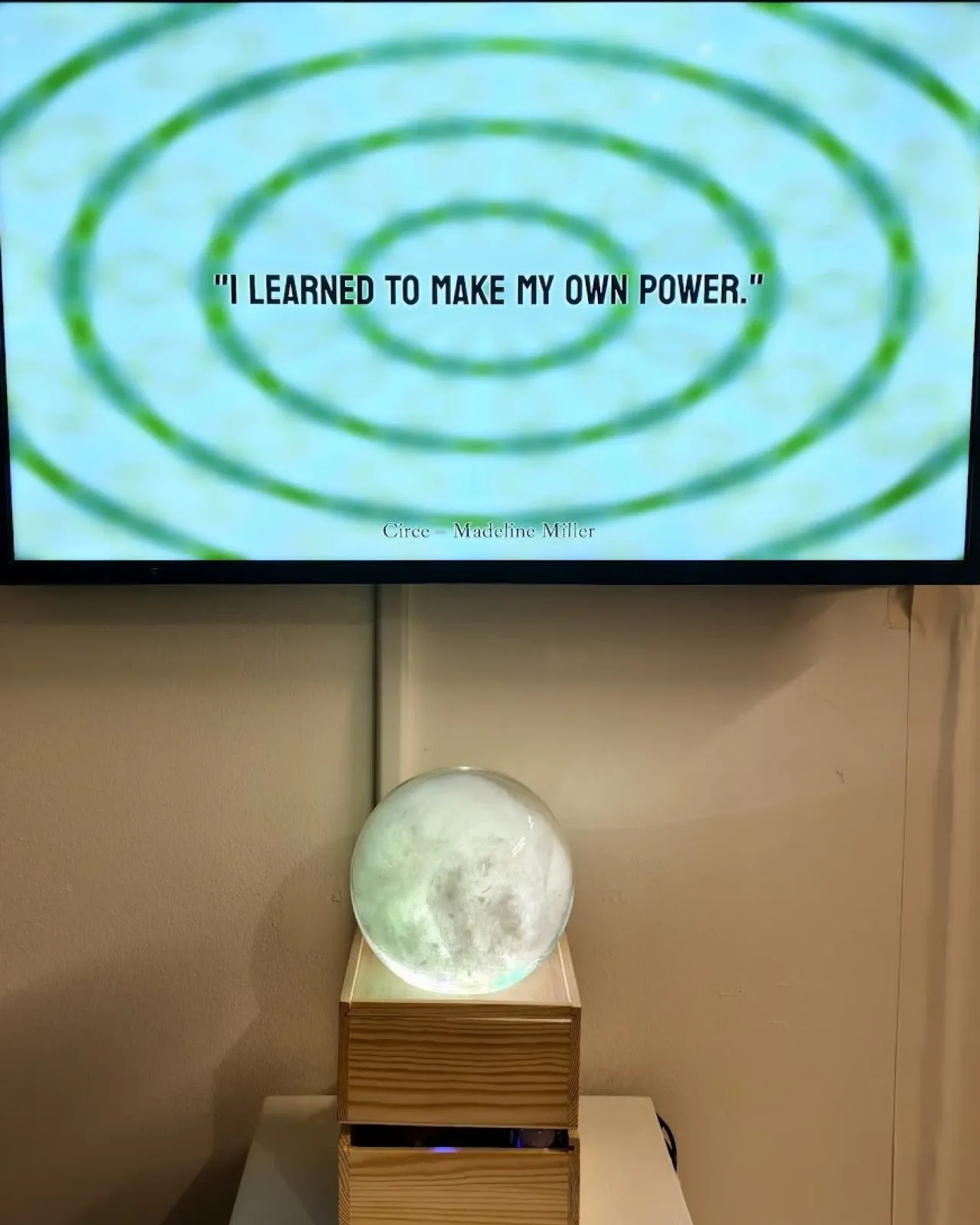 Illuminated crystal ball in a wooden enclosure beneath a green circular moving image.