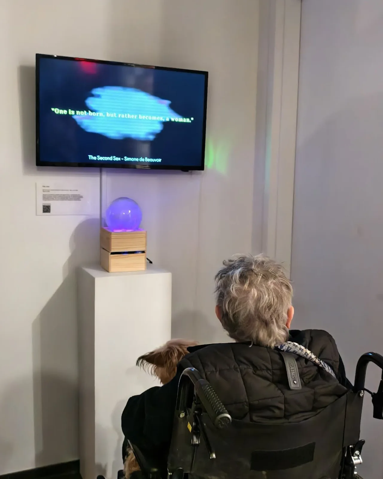 Seated visitor facing the violet-lit crystal and accompanying moving image at Pen + Brush.