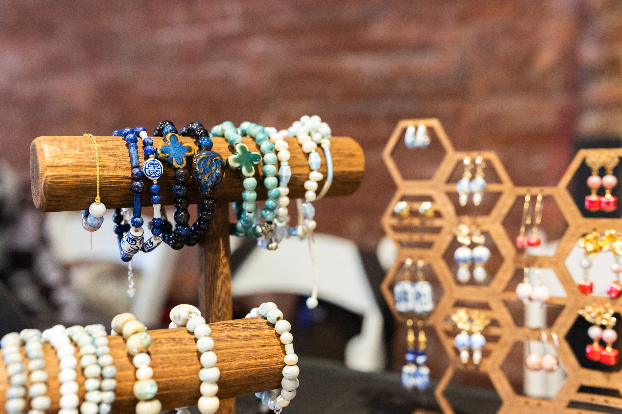 Close-up of handmade jewelry on a wooden display against a blurred brick wall